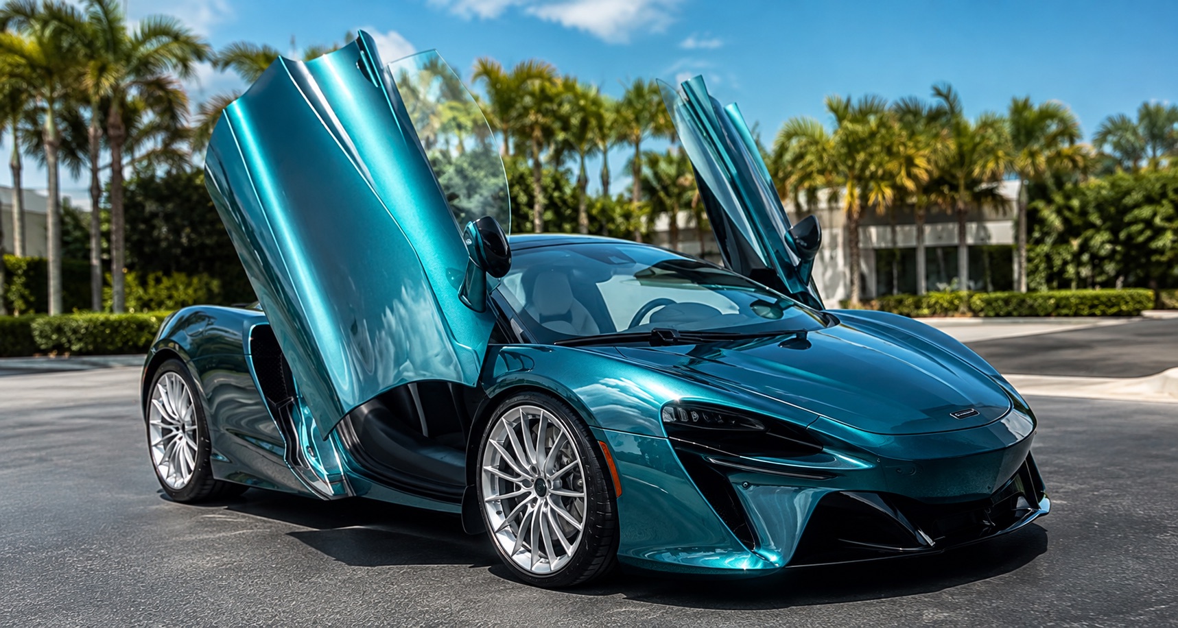 A teal McLaren Artura with dihedral doors raised, detailed to a mirror finish under Central Florida palms